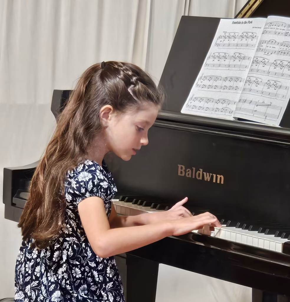 Young K&M Music School student concentrating on playing piano from sheet music.
