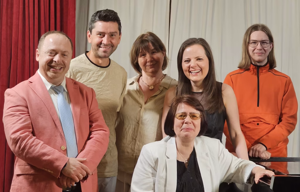 Smiling group photo of K&M Music School faculty and students on stage, representing the school community.