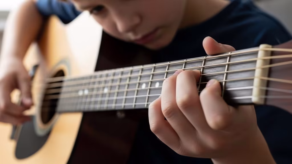 Close-up of a child’s fingers pressing guitar strings.