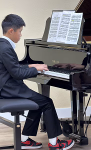 A student in a suit performing piano at a spring recital with sheet music on the stand