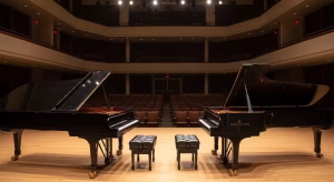 Two grand pianos on a professional recital hall stage in San Diego with audience seating in the background